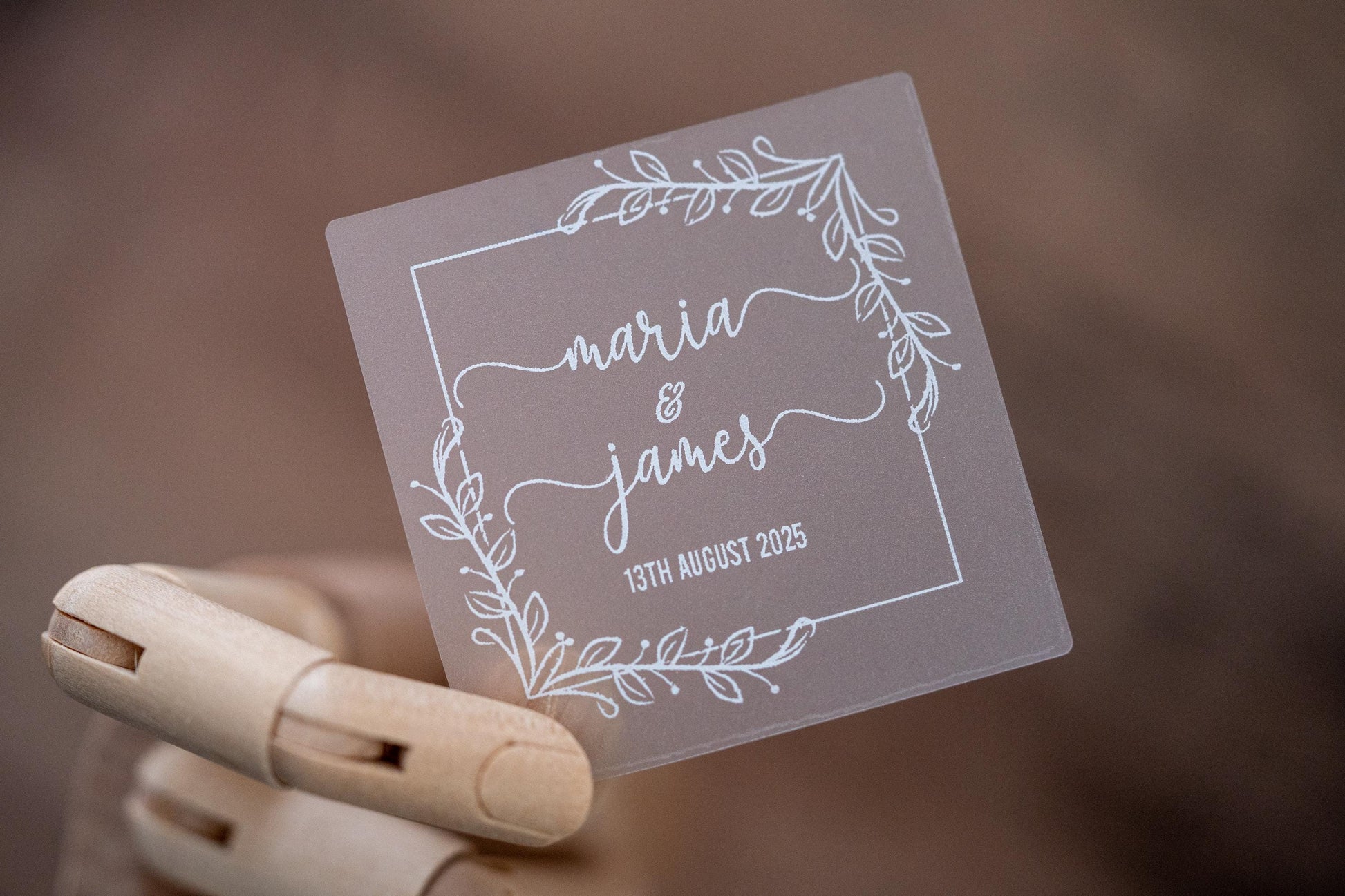 Frosted clear square sticker with a leaf square border. The names of the happy couple sit in the middle of the sticker using a lovely handwritten font. The wedding date finishes the sticker, the sticker is printed using a lovely white ink.