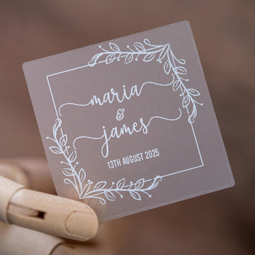 Frosted clear square sticker with a leaf square border. The names of the happy couple sit in the middle of the sticker using a lovely handwritten font. The wedding date finishes the sticker, the sticker is printed using a lovely white ink.