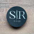 A custom monogram sticker on a black sticker with white print. The initials sit in the centre separated by a leaf line and finished with a date at the bottom.
