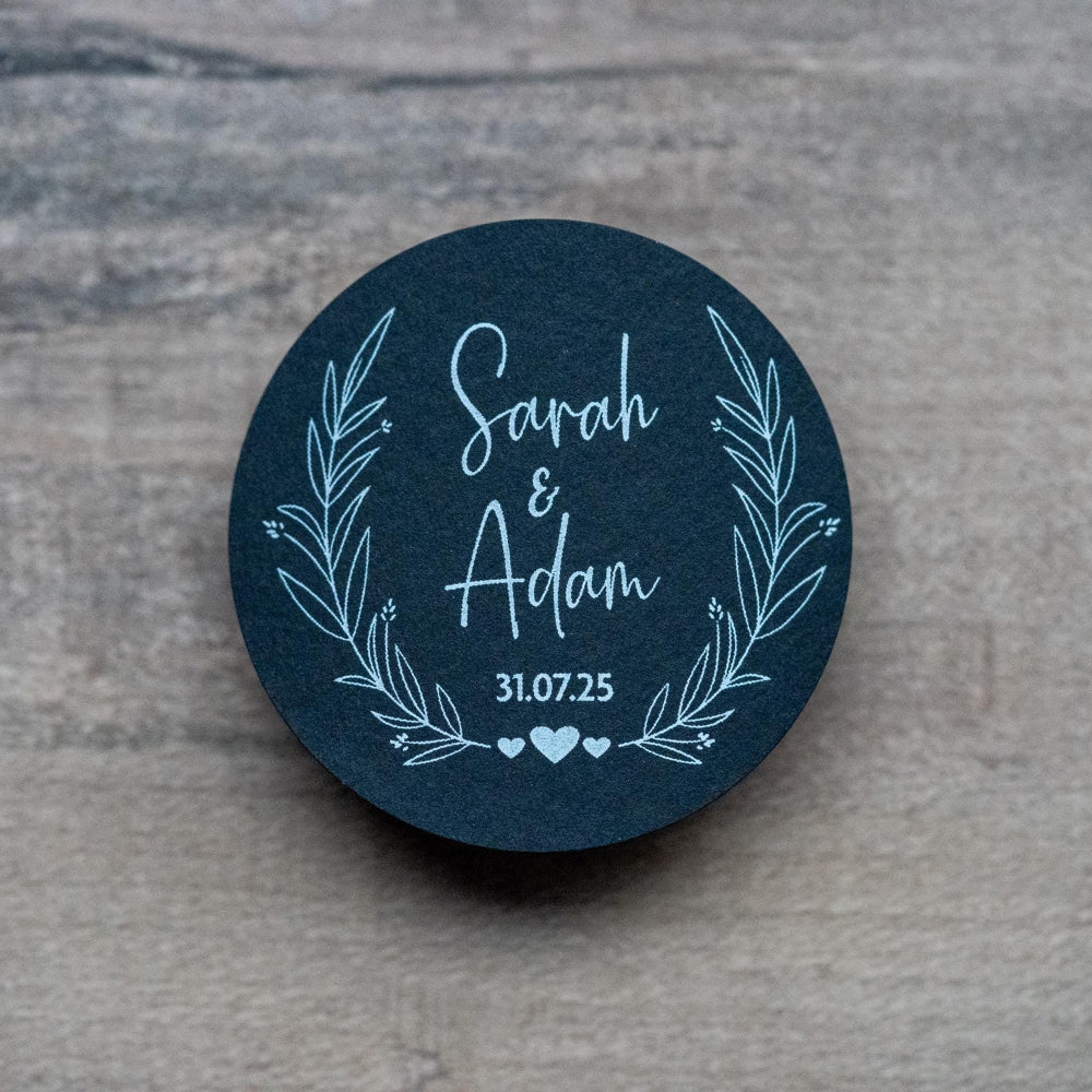 A black sticker with a leaf frame around the edges of the sticker. The name of the happy couple in the centre of the sticker with the wedding date underneath. The sticker is finished with three small hearts to symbolise everlasting love.