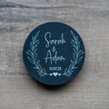 Round black sticker with 'Sarah & Adam' and date inside a leaf frame