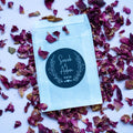 Personalised glassine envelope with a custom black sticker, surrounded by dried pink rose petals on a white background.