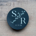 Round black sticker with 'SR' initials and date on a light wood surface