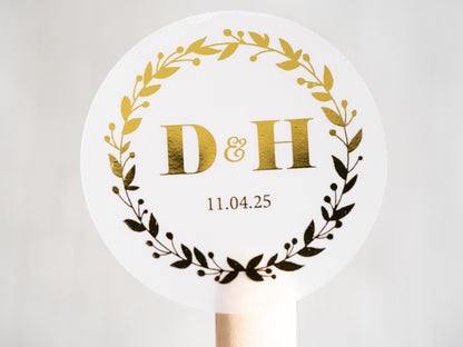 A personalised foil monogram sticker with a round leaf border. In the middle are the initials of the couple with the date of the special day underneath. The sticker is finished with a gold foil layer for added shine.