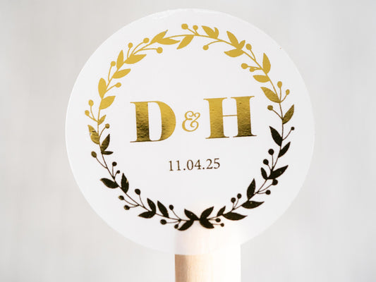 A personalised foil monogram sticker with a round leaf border. In the middle are the initials of the couple with the date of the special day underneath. The sticker is finished with a gold foil layer for added shine.