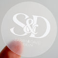 A clear sticker with monogram letters in the middle printed on white ink. The names of the happy couple and the wedding date sit underneath the letters to finish the sticker off.