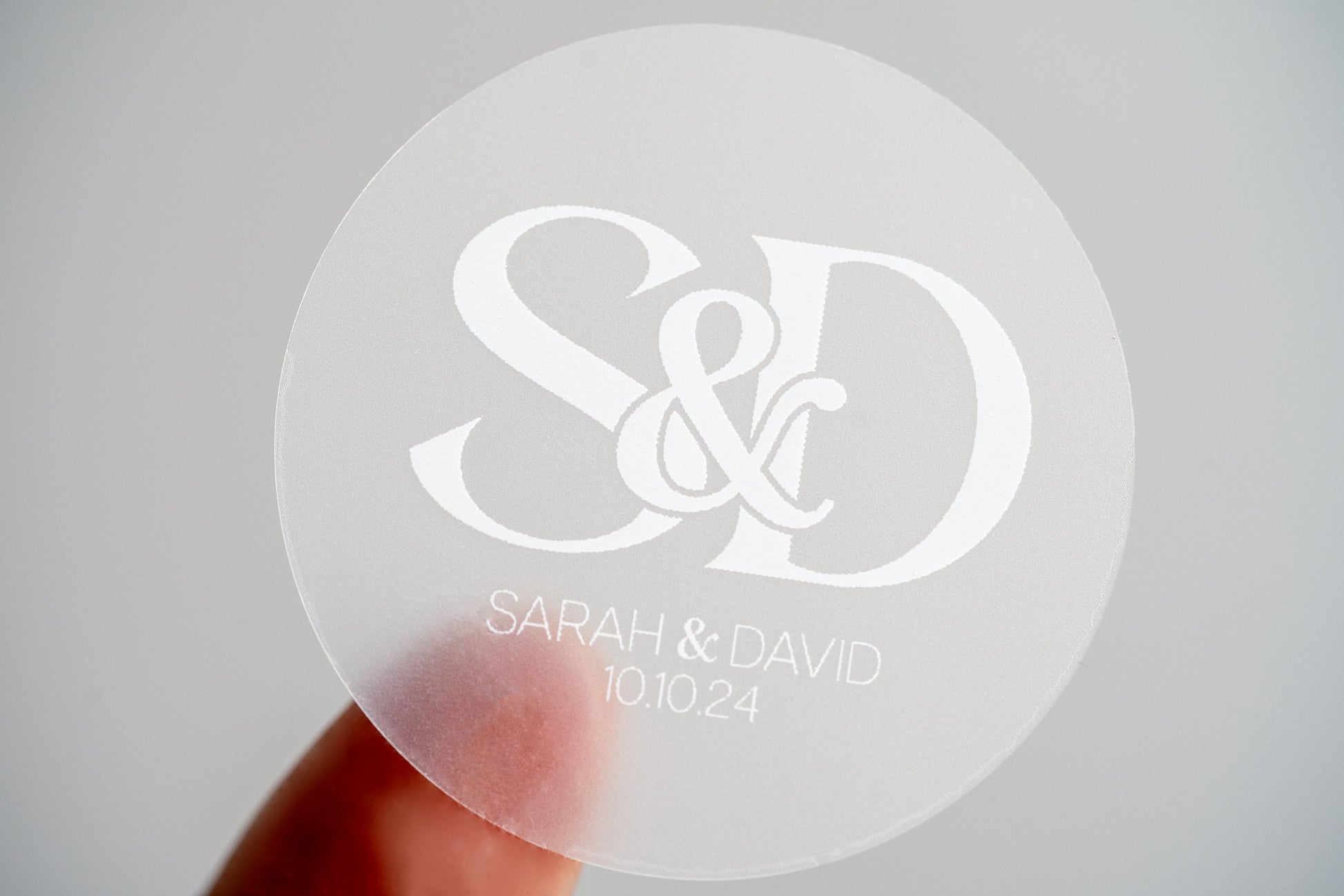 A clear sticker with monogram letters in the middle printed on white ink. The names of the happy couple and the wedding date sit underneath the letters to finish the sticker off.