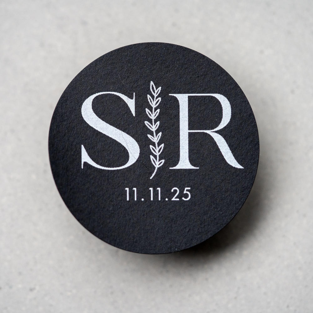A custom monogram sticker on a black sticker with white print. The initials sit in the centre separated by a leaf line and finished with a date at the bottom.