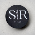 A custom monogram sticker on a black sticker with white print. The initials sit in the centre separated by a leaf line and finished with a date at the bottom.