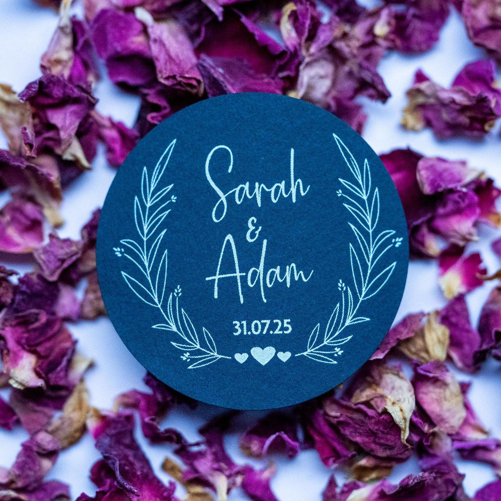 A black sticker with a leaf frame around the edges of the sticker. The name of the happy couple in the centre of the sticker with the wedding date underneath. The sticker is finished with three small hearts to symbolise everlasting love.