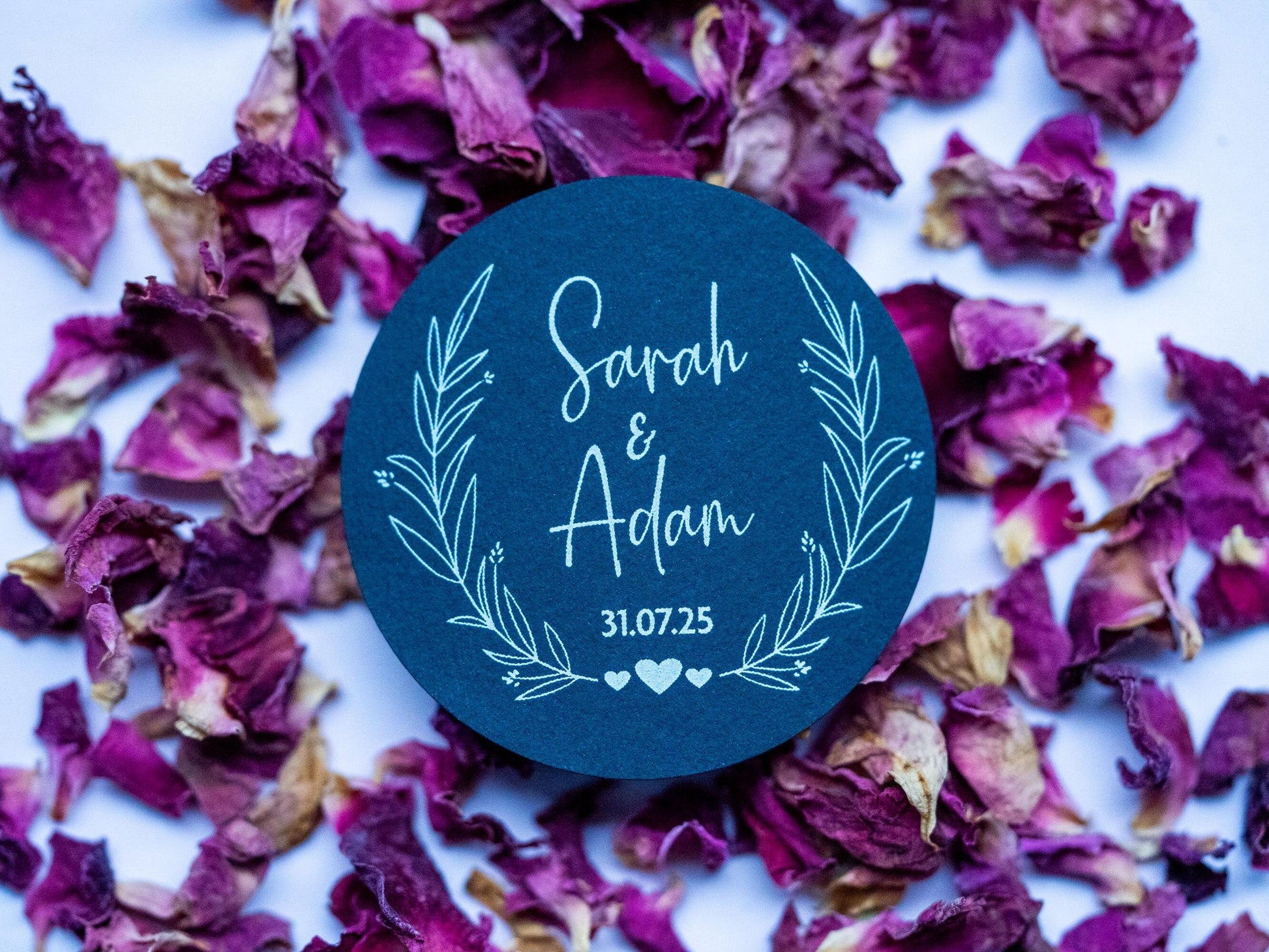 A black sticker with a leaf frame around the edges of the sticker. The name of the happy couple in the centre of the sticker with the wedding date underneath. The sticker is finished with three small hearts to symbolise everlasting love.