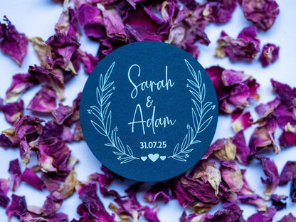 A black sticker with a leaf frame around the edges of the sticker. The name of the happy couple in the centre of the sticker with the wedding date underneath. The sticker is finished with three small hearts to symbolise everlasting love.