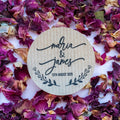Round kraft sticker with 'Maria & James' and date on dried pink and purple flower petals