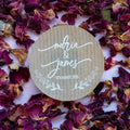 Round kraft sticker with 'Maria & James' and date on a bed of dried flowers