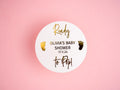 A round white sticker with gold foil text and accents, personalised with the name 'Olivia' and the words 'Baby Shower', against a pink background.