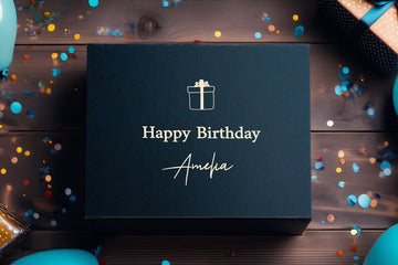 Black birthday gift box with 'Happy Birthday Amelia' text on a wooden surface with confetti.